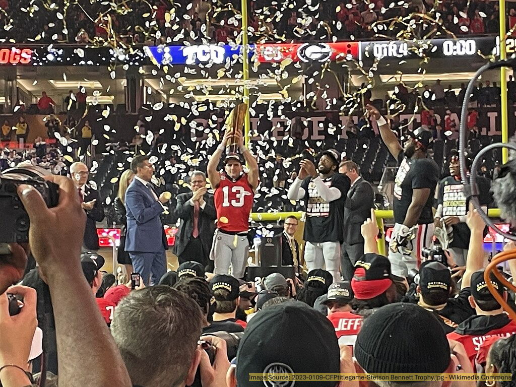 Football championship celebration with trophy presentation and falling confetti. A football player holds up the championship trophy as confetti falls during a celebration at a packed stadium. Teammates and officials stand nearby, while fans cheer in the background.